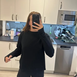 Träningströja med öppen rygg - Säljer en svart träningströja med öppen rygg. Tröjan har långa ärmar och en avslappnad passform. Perfekt för dig som vill ha en sportig och snygg look. Varmare bomullsmaterial