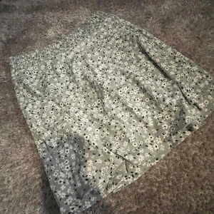 Ljusgrön blommig kjol - Supersöt ljusgrön kjol med små vita och svarta blommor. Kjolen har resår i midjan och är kort i modellen, men inte för kort. Aldrig andvänd & lappen sitter kvar.
