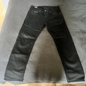 Svarta Levi's 502 jeans W32 L32 - Säljer ett par svarta Levi's 502 jeans med klassisk femficksdesign och raka ben. Jeansen har normal passform och är tillverkade i ett slitstarkt denimtyg. Perfekta för dig som gillar en tidlös och clean look. Dem har en liten fläck vid grenen som knappast syns kan tas bort enkelt.