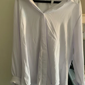 Vit klassisk skjorta - Säljer en stilren vit skjorta med klassisk krage och långa ärmar. Skjortan har dold knäppning framtill och är tillverkad i ett mjukt bomullstyg. Perfekt för en clean och enkel look.