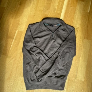 Brun tröja med halv dragkedja från Sand Copenhagen - Säljer en brun tröja från Sand Copenhagen med halv dragkedja och ståkrage. Tröjan har långa ärmar och ribbade muddar vid ärmslut och nederkant. Perfekt för lager-på-lager och snygg detalj med mönstrat tyg på insidan av kragen. Hör av dig vid åtankar!