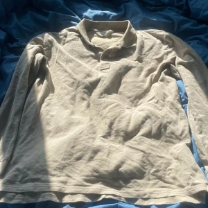 Beige pikétröja från H&M - Säljer en beige långärmad pikétröja från H&M. Tröjan har klassisk krage och knäppning vid halsen. Perfekt för en avslappnad och stilren look. Tillverkad i mjukt material som känns skönt mot huden.
