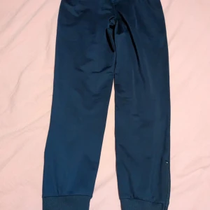 Mörkblå träningsbyxor från Errea - Säljer ett par mörkblå träningsbyxor från Errea med dragkedjor vid bensluten och fickor med dragkedja. Byxorna har resår i midjan och muddar vid anklarna. Perfekta för sport eller chill.