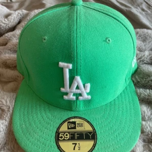 Grön LA-keps från New Era 59FIFTY - DISKUTERBART PRIS. Snygg grön keps från New Era 59FIFTY med LA-logga framtill i vitt. Klassisk modell med böjd skärm och broderade detaljer. Passar perfekt för dig som gillar sportig stil och vill sticka ut med färg. 
