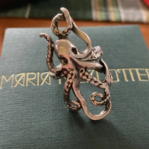 Maria Nilsdotter Bläckfiskring i silver från  - Unik och detaljerad ring i form av en bläckfisk, tillverkad i silver. Ringen har en cool och konstnärlig design med tydliga tentakler som slingrar sig runt fingret. Märkt med MNO på insidan. storlek 18,7 mm