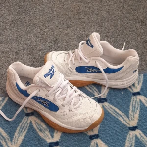 Vita och blå sneakers från Reebok - Säljer ett par klassiska vita sneakers från Reebok med blå detaljer och gummisula. Skorna har snörning och en sportig design med Reebok-logga på sidan och tungan. Perfekta för dig som gillar retrostil och bekväma skor .Skor är nästan nya. 