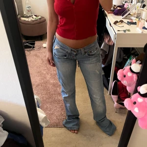 Lågmidjade ljusblå jeans med cut-out detaljer - Säljer ett par lågmidjade ljusblå jeans med unika cut-out detaljer vid höfterna. Jeansen har raka ben, klassiska fickor och slitningar framtill för en trendig look. Perfekta för dig som vill sticka ut med din stil.