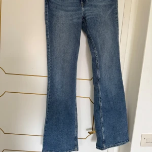 Blå bootcut jeans med hög midja - Säljer ett par klassiska blå bootcut jeans med hög midja från &Denim. Jeansen har en snygg tvätt och raka ben som släpper ut nertill. Perfekta för dig som gillar en tidlös och avslappnad stil.