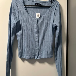 Ljusblå ribbad kofta  - Säljer en ljusblå ribbad kofta från GAP i storlek S. Tröjan har långa ärmar, u-ringning med dekorativ kant och knappar framtill. Perfekt att styla till jeans eller kjol för en fräsch look. Helt ny. 🩵