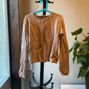 Beige kofta med knappar - Säljer en gammaldags rosa kofta med rund halsringning och knäppning framtill. Tröjan har långa ärmar och är i ett tunt, mjukt material som passar perfekt till lager-på-lager. Enkel och stilren design.