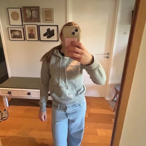 Grå hoodie med huva - Säljer en enkel och stilren grå hoodie med huva och dragsnören. Tröjan har lång ärm och en klassisk känguruficka framtill. Perfekt för en avslappnad look och passar till det mesta. Säljer då den är för liten! Skriv gärna om du undrar något