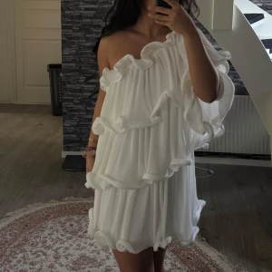 Vit oneshoulder volangklänning - Säljer en superfin vit kortklänning med oneshoulder och stora volanger. Klänningen har en luftig och flowy passform med flera lager volanger som ger en unik och trendig look. Perfekt för dig som vill sticka ut och älskar statement-plagg!