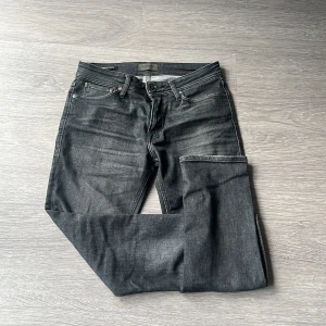 Mörkgrå jeans från Jack&Jones - Snygga mörkgrå jeans från Jack & Jones, modell Clark Regular. Klassisk femficksdesign med raka ben och normal passform. Jeansen har subtila slitningar och är tillverkade i mjukt denimtyg som sitter skönt hela dagen. Perfekt för dig som gillar stilrena och tidlösa jeans. Jeansen är helt ny och använda en gång