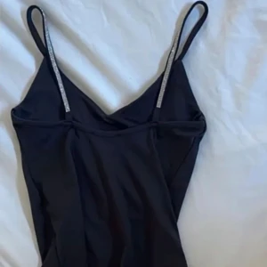 Svart bodysuit med strassband Amisu - Svart bodysuit från Amisu med smala axelband dekorerade med strass för extra bling. V-ringad framtill och figurnära passform som ger en snygg siluett. Perfekt för att lyfta din outfit med lite extra glam.