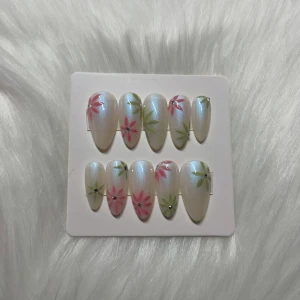 Pärlemor naglar med blommor - Snygga lösnaglar i pärlemor med handmålade blommor i rosa och grönt samt små silverdetaljer. Naglarna har en elegant, oval form och kommer i ett set om tio stycken. Perfekt för dig som vill ha en unik och färgglad nageldesign.