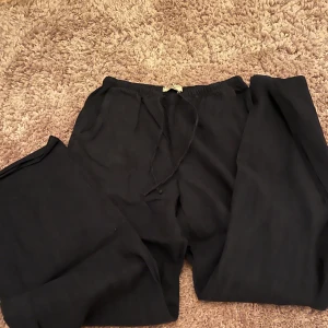 Marinblå linnebyxor från Gina Tricot - Marinblå linnebyxor från Gina Tricot med avslappnad passform och snörning i midjan. Byxorna har raka ben och är tillverkade i ett lätt och luftigt linnematerial, perfekta för en chill och stilren look.