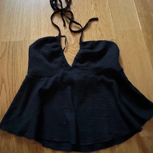 Svart halterneck linnetopp - Snygg svart linnetopp med halterneck och v-ringning. Toppen har en lätt utsvängd nederdel och knytband i nacken.