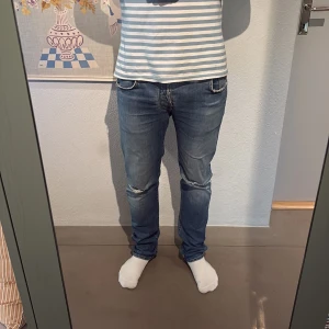 Blå jeans från Jacob Cohen med slitningar - Snygga blå jeans från Jacob Cohen med coola slitningar vid knäna och klassisk femficksdesign. Jeansen är i fint skick med undantaget att det finns ett litet hål inuti fickan som ej syns, byxorna är strl 33