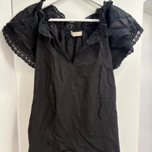 Svart blus med spets från Vanessa Bruno - Supersnygg svart blus från Vanessa Bruno med broderade detaljer framtill och v-ringad hals. 