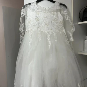 Vit barnklänning med spets från Fiona & Co  - Barnklänning med spetsärmar och blommig broderad överdel dekorerad med pärlor. Ny med prislapp aldrig använt 