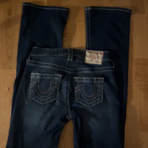 True Religion blå bootcut jeans - mörkblåa true religion jeans med rosa söm på fickorna, inte använt mycket. strl 24x32 nypris 1199kr