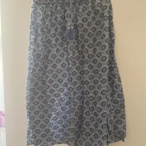 Blå långkjol med mönster och snörning - Säljer en blå långkjol med snyggt geometriskt mönster i mörkblått och vitt. Kjolen har en bekväm midja med snörning och tofsar som detalj. Perfekt för dig som gillar boho-vibe och vill ha något luftigt och stilrent till sommaren. Den är i storlek 170 men passar dig som är mellan 160-170!