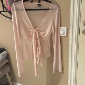 Ljusrosa omlottopp från Gina Tricot - Supersöt ljusrosa omlottopp från Gina Tricot i tunn och mjuk polyester. Toppen har lång ärm, v-ringning och snygg knytning framtill som ger en chill och feminin vibe. Perfekt att styla med jeans eller kjol för en trendig look.