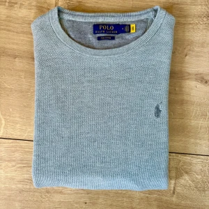 Ljusgrå tröja från Polo Ralph Lauren - Snygg ljusgrå tröja från Polo Ralph Lauren i mjuk pima bomull. Klassisk rund hals och diskret broderad logga på bröstet. Långärmad med ribbade muddar och nederkant, perfekt för chill höst- och vårväder.