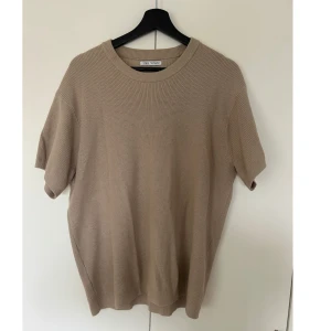 Beige stickad t-shirt från Zara - Snygg beige stickad t-shirt från Zara med rund hals och korta ärmar. T-shirten har en loose passform och är tillverkad i mjukt stickat material som ger en chill och avslappnad vibe. Perfekt för dig som gillar enkel och stilren design.
