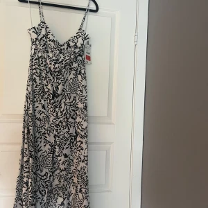 Vit och svart långklänning från Zara - Säljer en snygg långklänning från Zara i storlek XS. Klänningen är vit med svart blommigt mönster, har smala axelband och v-ringad hals. Materialet är lätt och luftigt, perfekt för varma dagar. Passformen är normal och klänningen har en elegant siluett.