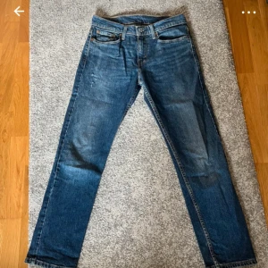 Levi's 502 blå jeans W29 L30 - Säljer ett par klassiska Levi's 502 jeans i snygg blå tvätt. Modellen har raka ben och normal passform, med fem fickor och ikonisk läderpatch bak. Jeansen är tillverkade i slitstarkt bomullsdenim och har den typiska röda Levi's-taggen vid bakfickan.