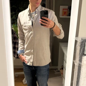 Beige bomullsskjorta med knappar - Snygg beige skjorta i mjuk bomull med klassisk button-down krage och bröstficka. Långärmad modell med ljusa knappar och diskret struktur i tyget. Perfekt för dig som gillar stilrena och enkla plagg. Passar dig som vill ha en normal passform.