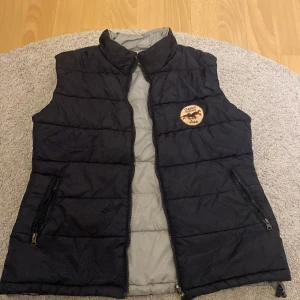 Svart dunväst med dragkedja - Svart quiltad dunväst från Classic Running Wear med hög krage och två fickor med dragkedja. 