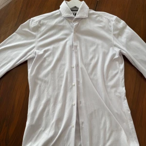 Vit slim fit skjorta från BOSS - Snygg vit skjorta från BOSS Performance i slim fit-modell. Skjortan har klassisk krage och är tillverkad i mjuk bomull och polyester som känns skön mot huden. Perfekt för dig som gillar stilrena och moderna plagg.