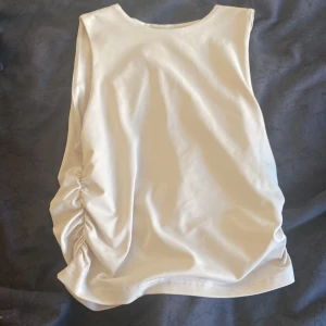 Beige ärmlös linnetopp med snörning - Snygg beige linnetopp med ärmlös design och cool snörningsdetalj på sidan som ger en unik look. Toppen har rund hals och är gjord i mjukt material som känns skönt mot huden. Perfekt för dig som gillar stilrena plagg med en twist.