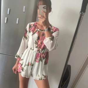 Vit blommig jumpsuit med långa ärmar - Supersöt kort jumpsuit från DM retro, med elastisk midja som ger en skön passform. Luftigt material, perfekt för sommaren. Snygg och fräsch look! Använd någon enstaka gång, men fortfarande i nyskick. 