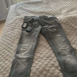Grå distressed jeans från Dsquared2 - Säljer ett par grå jeans från Dsquared2 med coola slitningar och trasiga detaljer på både fram- och baksida. Jeansen har fem fickor, normal passform och klassisk knappgylf. Materialet är mjukt jeans och färgen är snyggt tvättad för en edgy look. Snabbpris!!!!!!