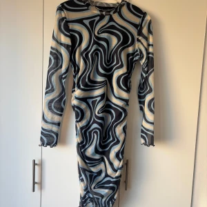 Mönstrad klänning från Vero Moda - Säljer en långärmad klänning från Vero Moda i storlek M. Klänningen har ett coolt mönster i svart, beige och ljusblått, med tight passform och rynkade detaljer längs sidan 