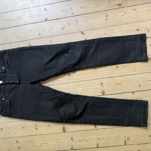Svarta jeans från Tramarossa, stl 31 - Säljer ett par svarta jeans från Tramarossa i storlek 31. Byxorna har raka ben, klassisk femficksdesign och snygga detaljer med röda sömmar och metallknappar. Materialet är en stretchig bomullsblandning för extra komfort. Tyvärr är lappen på baken borta.