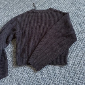Svart croppad stickad tröja - Säljer en svart croppad stickad tröja med ribbad struktur och långärmade ärmar. Tröjan har en enkel, rund halsringning och är perfekt för dig som gillar en chill och trendig stil. Passar snyggt till jeans eller kjol. Lite nopprig💕