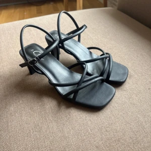 Svarta öppna klackskor  - Säljer svarta öppna klackskor med spänne och ”slingback” i storlek 39, från Clou (köpta från Din Sko). Skorna är knappt använda och i väldigt bra skick, endast ett lite märke framtill på högra skon (se sista bilden). Klacken är ca. 5cm hög och bred. Väldigt bekväma.