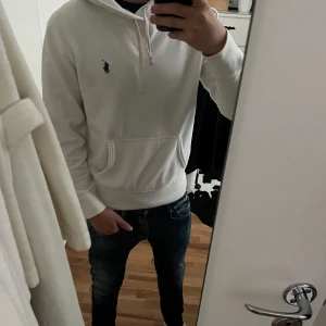Vit hoodie från Ralph Lauren - Säljer en clean vit hoodie från Polo Ralph Lauren med klassisk blå logga på bröstet. Tröjan har huva med snörning, stor magficka och långa ärmar. Mjuk bomullskvalitet som är skön att ha på sig. Perfekt till jeans eller joggers för en chill look. Den har en liten defekt på armen fast den tänker man inte på därav säljer ja den lite billigare. Använd gärna PostNord som frakt då Instabox ligger en bit ifrån mig. Leverarar inom 24h✅