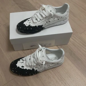 Paintsplatter gata maison margiela - Maison Margiela sneakers i vitt med svart färgstänk-design. Skorna har rund tå, snörning och platt sula. Tillverkade i tyg och har en unik, konstnärlig look som sticker ut. Kommer med originalkartong och dustbags. Perfekt för dig som gillar statement pieces. Kvitto finns fråga privat för det 🤛🏻👍🏻