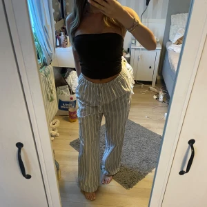 Randiga linnebyxor med snörning - Säljer ett par chill randiga linnebyxor i vitt och blått med breda ben och skön snörning i midjan. Perfekta för varma dagar och har en loose passform som gör dem superbekväma. Passar dig som gillar avslappnad stil och vill ha något luftigt. Oanvända!