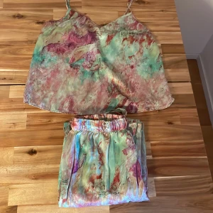 Färgglad linnetopp med abstrakt mönster - Säljer en linnetopp med tunna axelband och v-ringning. Toppen har ett unikt abstrakt mönster i ljusa toner av rosa, grön, röd och beige. Materialet känns mjukt och svalt, perfekt för varma dagar. Passformen är loose och toppen är ärmlös.