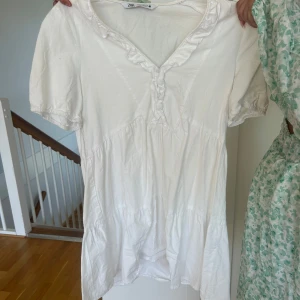 Vit kort klänning från Zara - Säljer en söt vit klänning från Zara volangdetaljer vid halsringningen. Använd fåtal gånger.