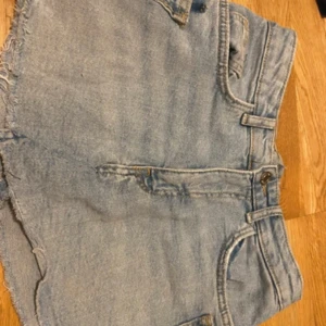Ljusblå jeanskjol - Snygga ljusblå jeanskjol med låg midja och rå, fransig kant nedtill. Klassisk femficksmodell med knapp och dragkedja framtill. Shortsen har slitna detaljer och är gjorda i ett robust denimtyg som ger en cool och avslappnad vibe.