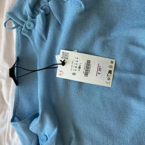Ljusblå stickad topp från ZARA - Supersöt ljusblå stickad topp från ZARA med lång ärm och snygga knapprader längs axlarna. Rund halsringning och figurnära passform som sitter riktigt snyggt. Perfekt att styla med jeans eller kjol för en chill look.