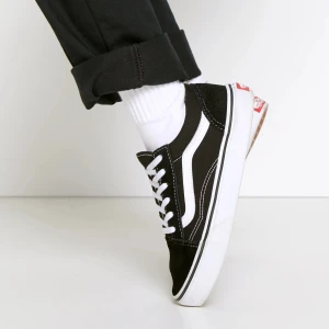 Svarta Vans Old Skool sneakers - Klassiska Vans Old Skool sneakers i svart med vit sula och vit sidostripes. Skorna har snörning och en platt sula, tillverkade i mocka och canvas. Perfekt för dig som gillar streetstyle och vill ha en tidlös look.