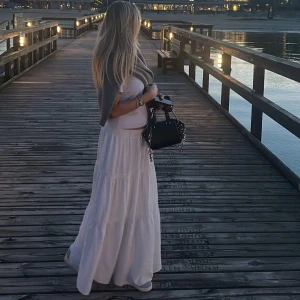 Vit långkjol med volanger - Säljer en superfin vit långkjol med flera volanger och skön resår i midjan. Kjolen har en luftig och flowy känsla, perfekt för varma dagar. Den är enkel att matcha med både crop tops och stickade tröjor. Materialet känns lätt och bekvämt mot huden.